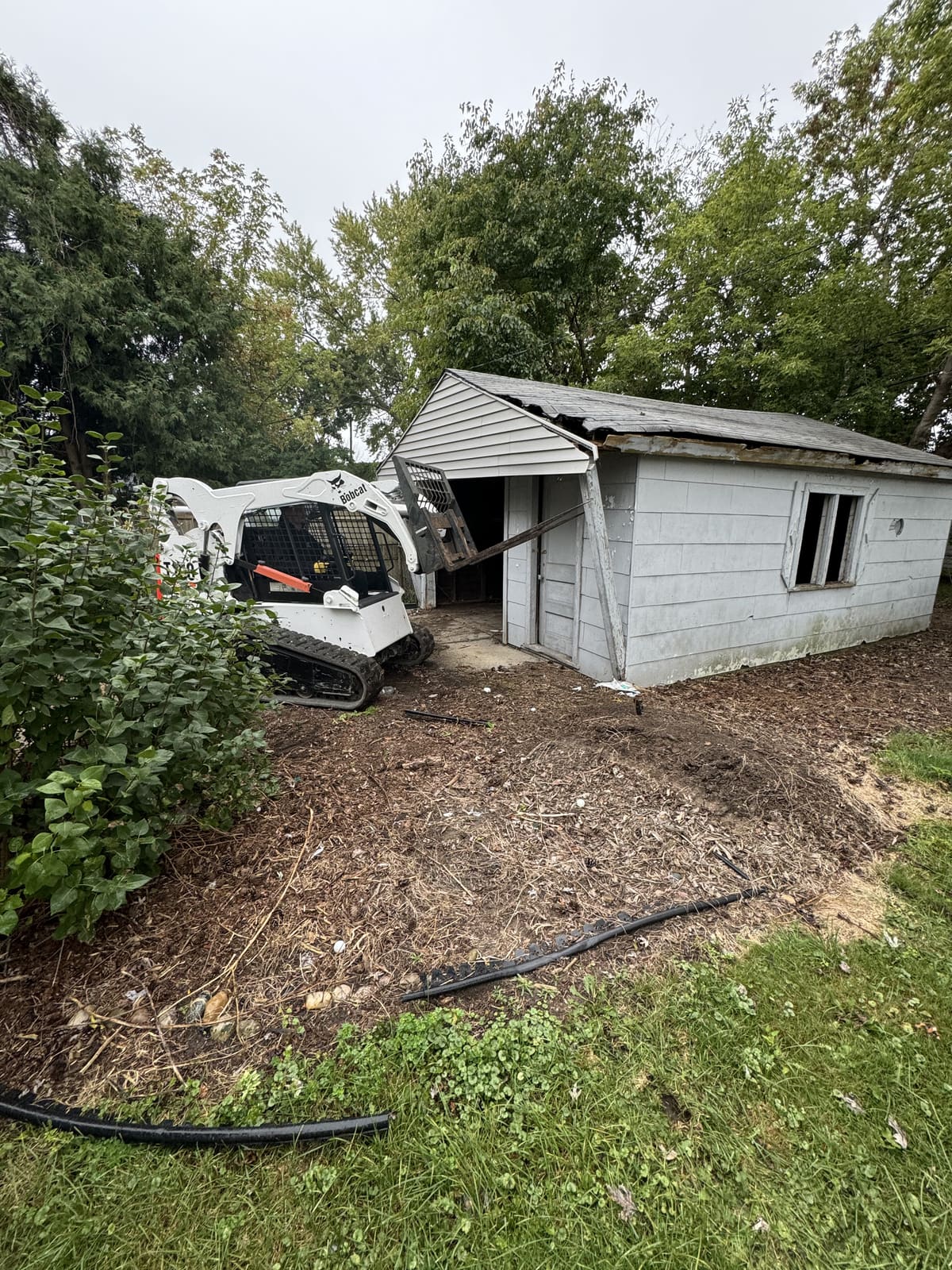 Bobcat skid steer parked in front of a detached garage before demolition