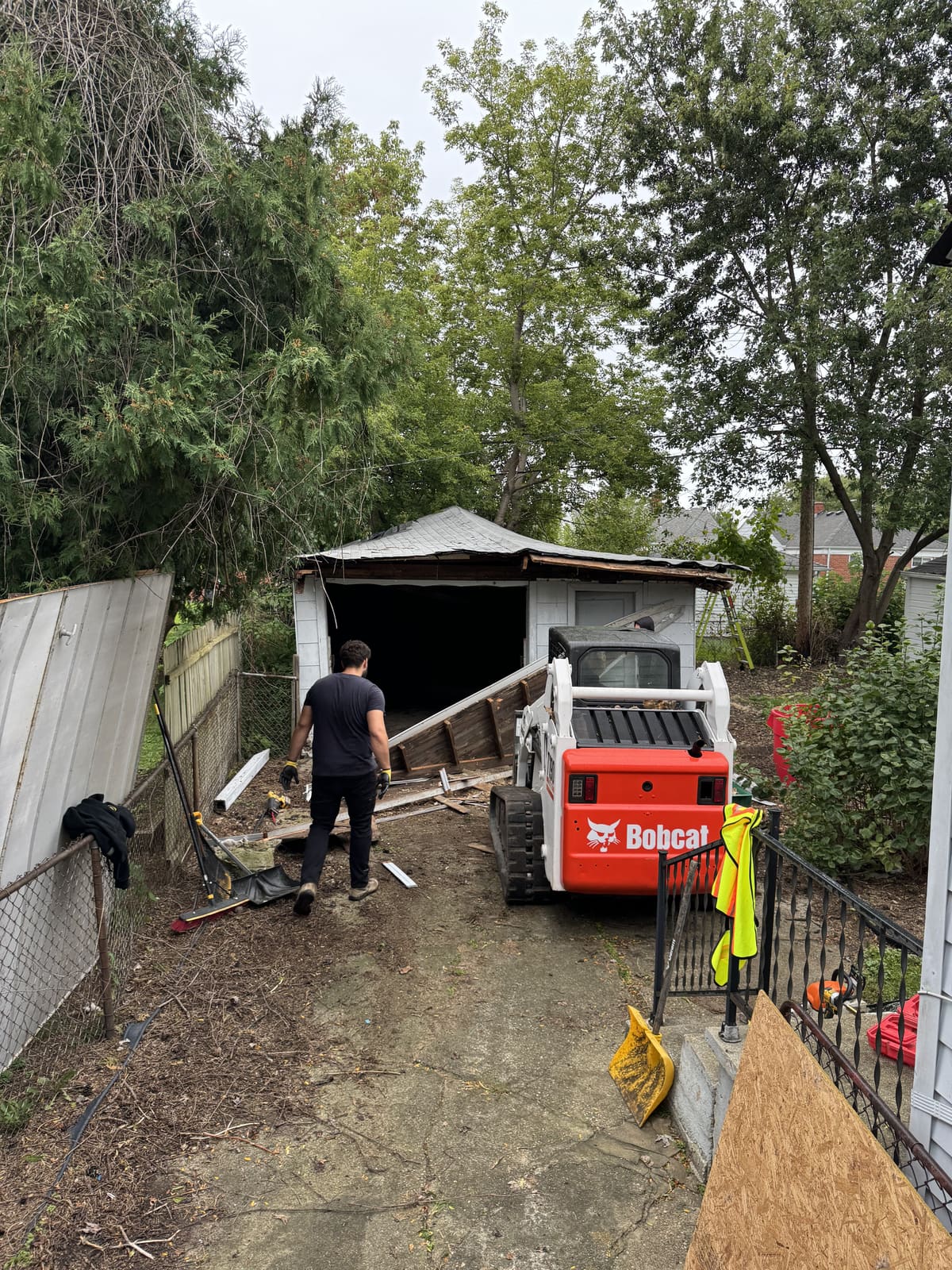 Crew member and a Bobcat working a backyard garage demolition