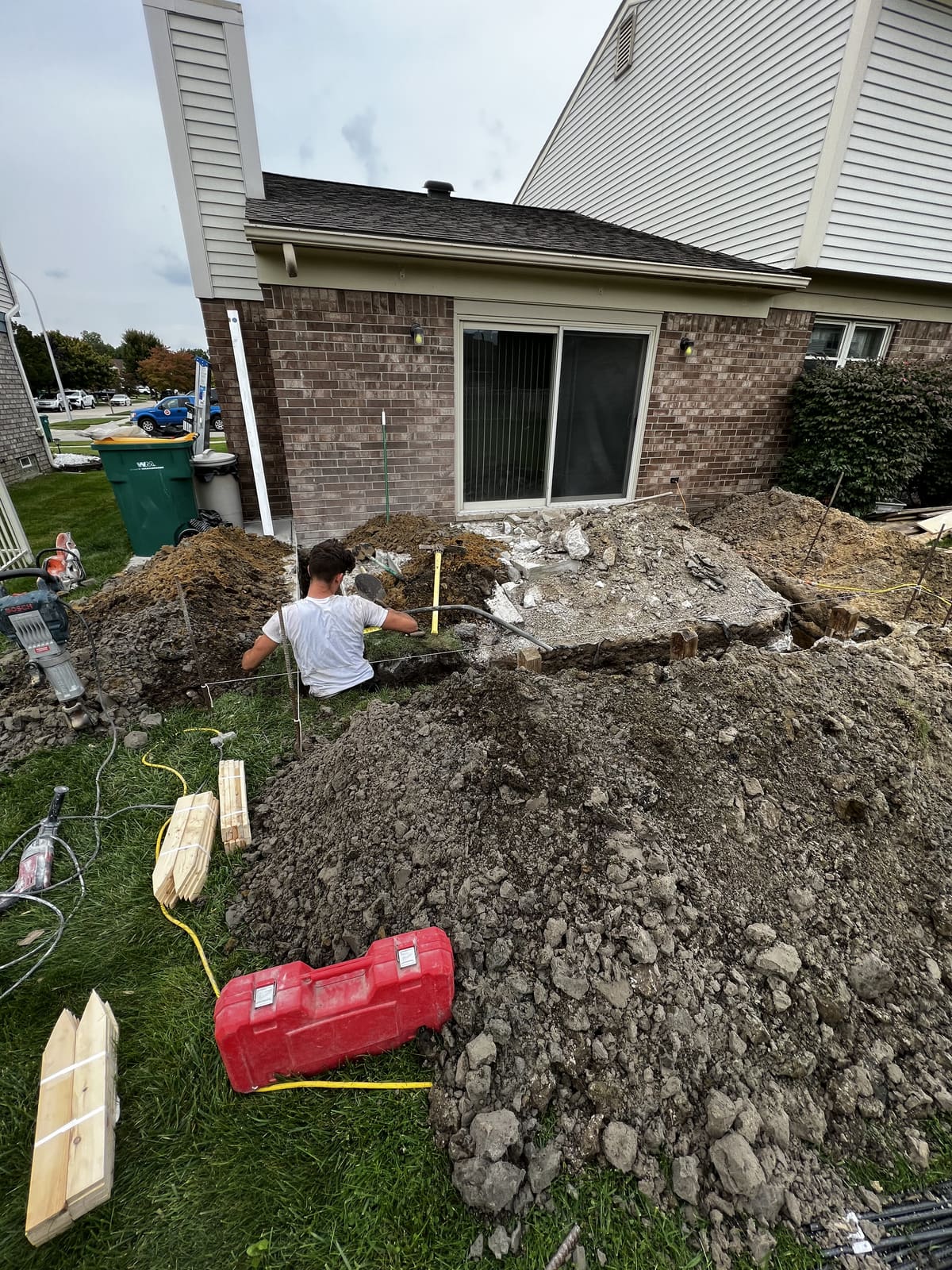 Worker clearing soil and debris beside a brick house foundation
