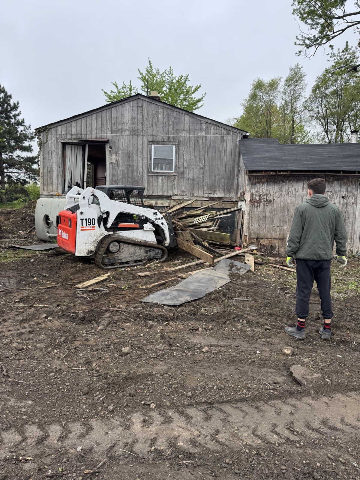 Skid steer beside a weathered outbuilding ready for demolition