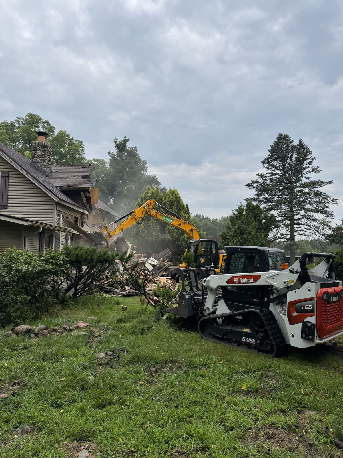 Excavator and skid steers tearing down a house