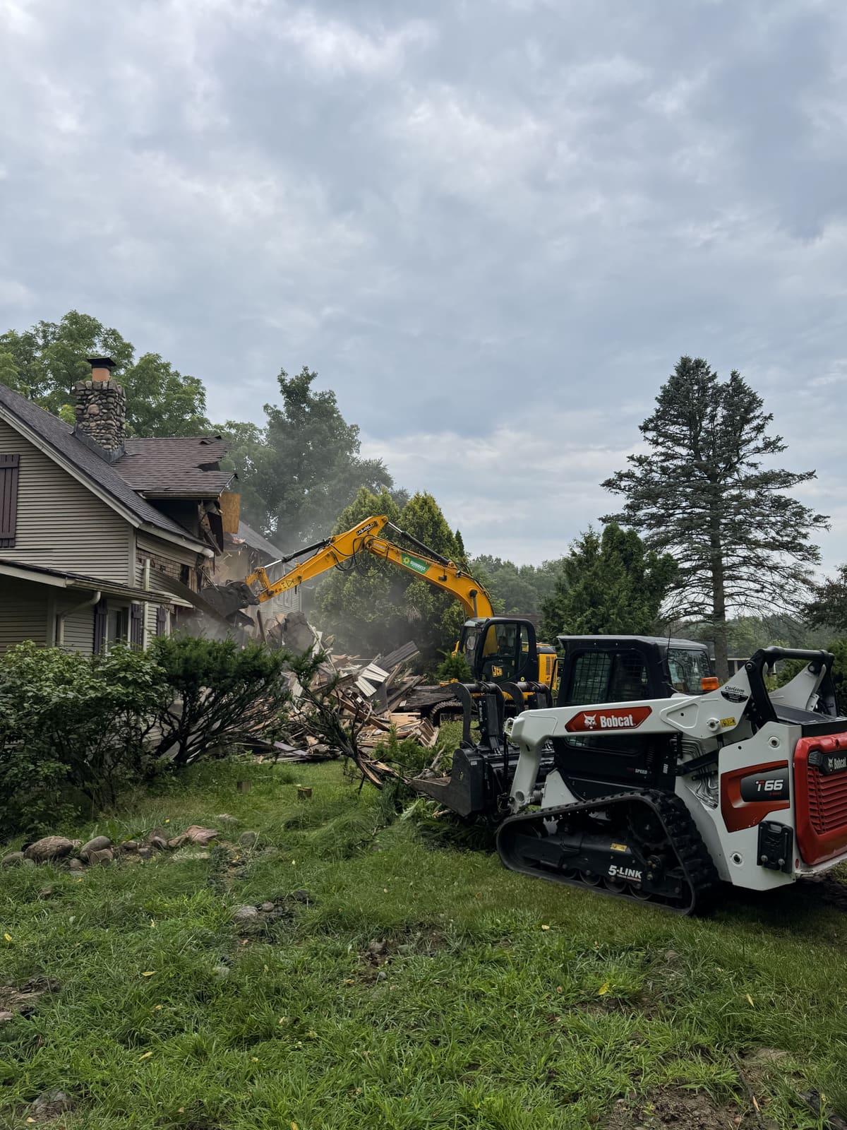 House demolition in progress with an excavator and two skid steers
