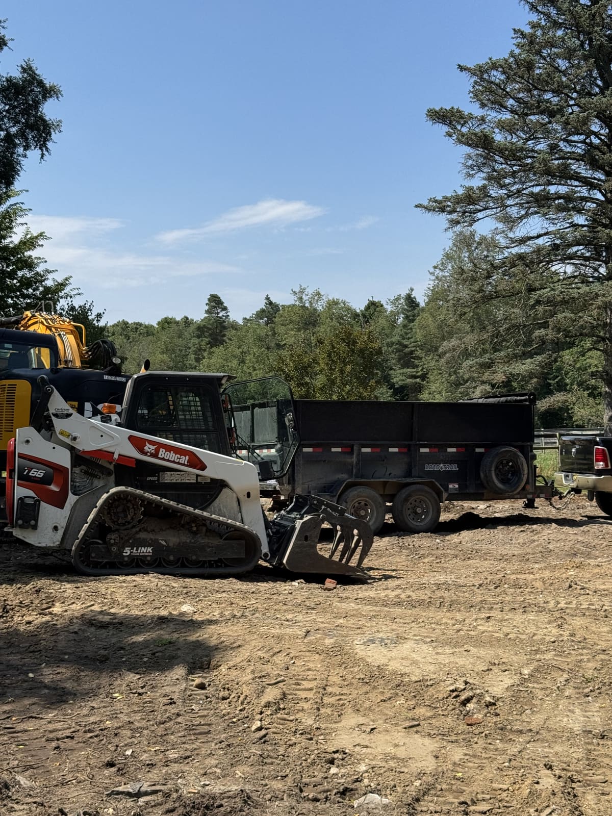 Bobcat loading a dump trailer on a cleared jobsite